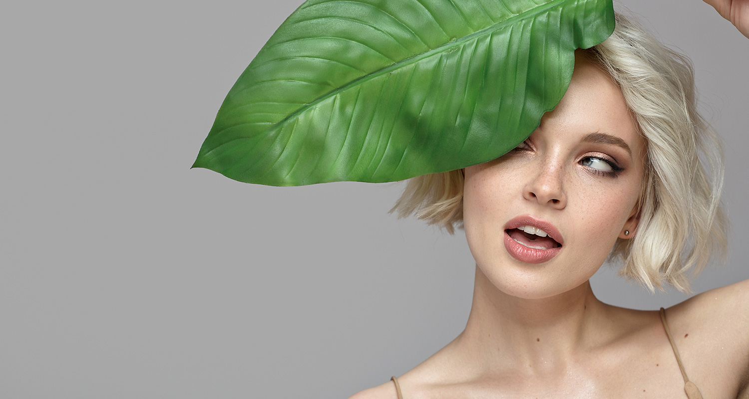 Porträt einer jungen Frau mit einem großen grünen Blatt seitlich im Gesicht