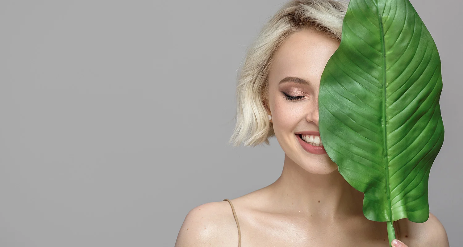 Frau versteckt ihr Gesicht hinter einem großen Blatt.